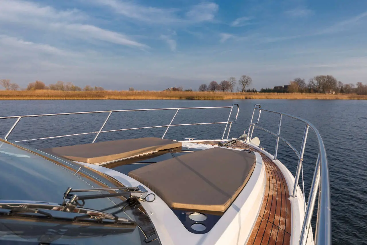 View from the bow of a modern motorboat showcasing sunbeds, a calm river, and lush green foliage under a clear sky.