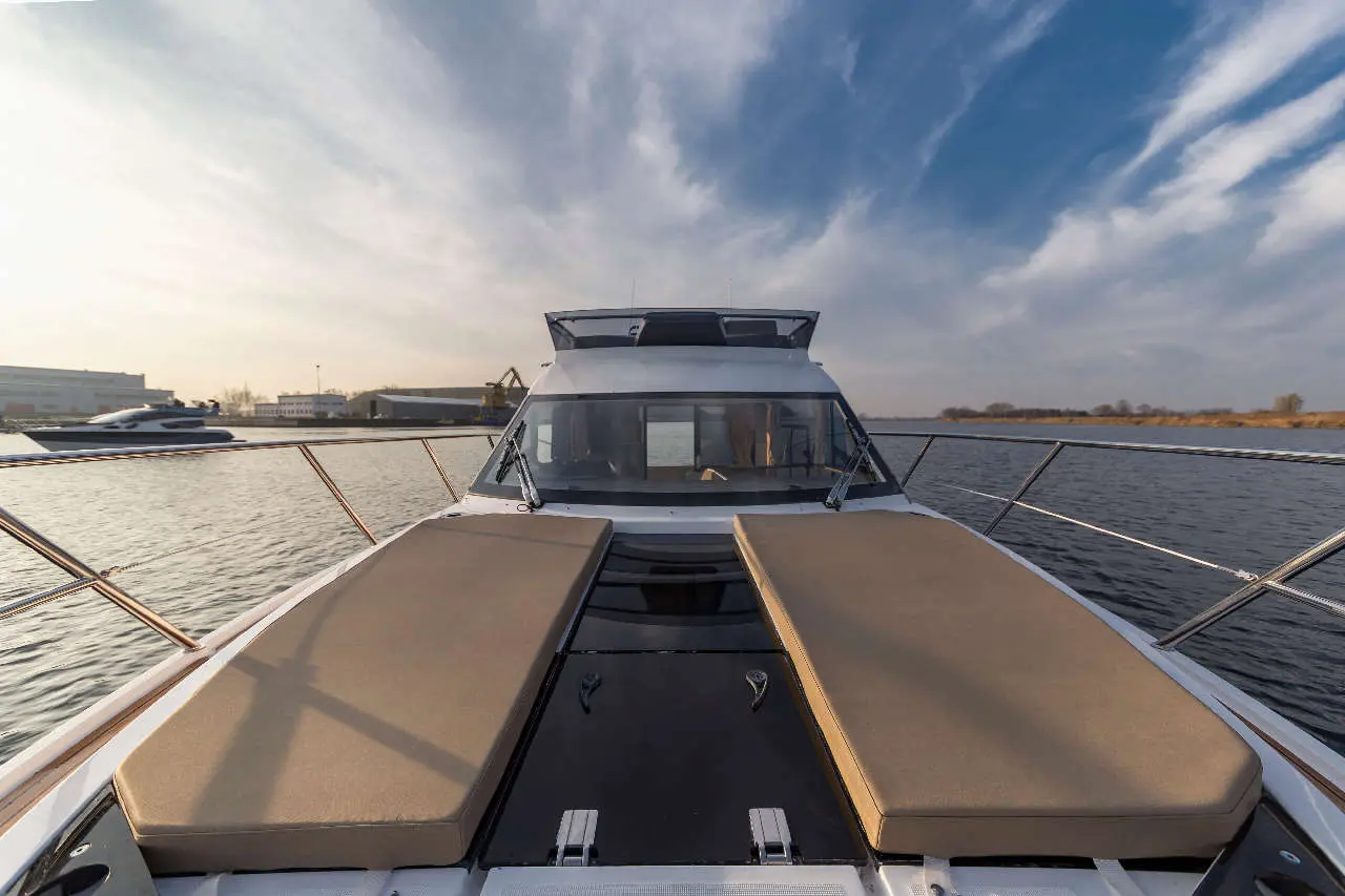 View from the bow of a luxury boat, showcasing two sun loungers, calm water, and a cloudy sky in the background.