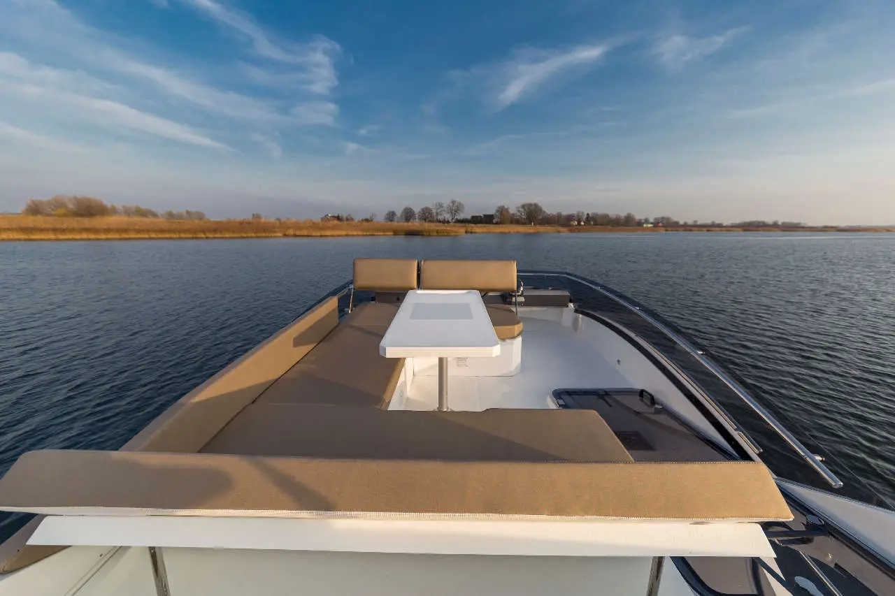 View from the back of a boat featuring a white table and cushioned seating against a serene water landscape.