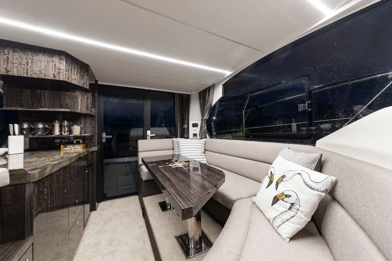 Luxurious yacht interior with sleek cabinetry, plush seating, and a unique decor pillow featuring swans, illuminated by soft lighting.