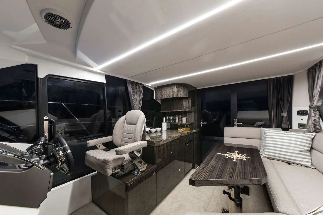Modern boat interior featuring a captain's chair, steering wheel, cabinet, and a seating area with a decorative table.
