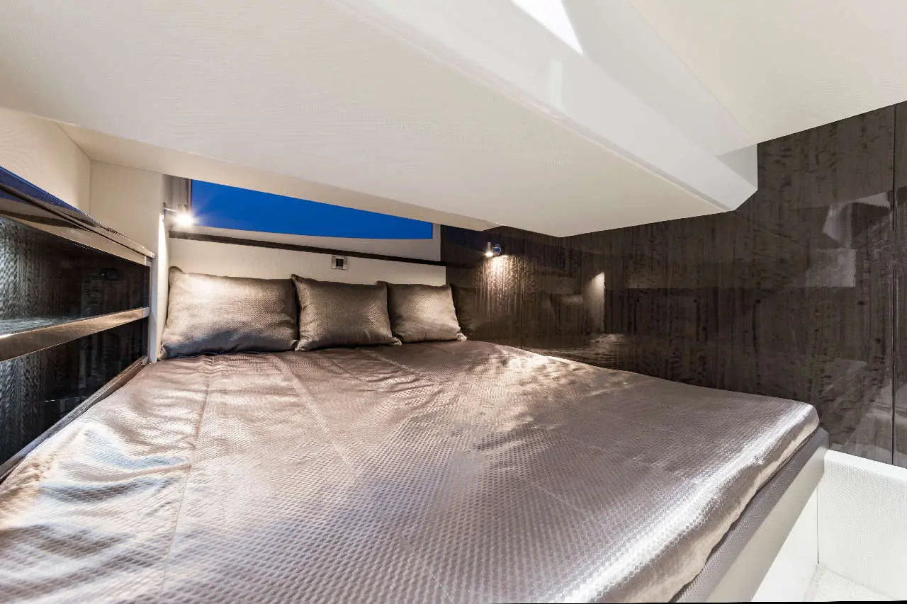 A modern, well-lit bedroom features a large bed with plush cushions and a sleek design, set against a dark wall.