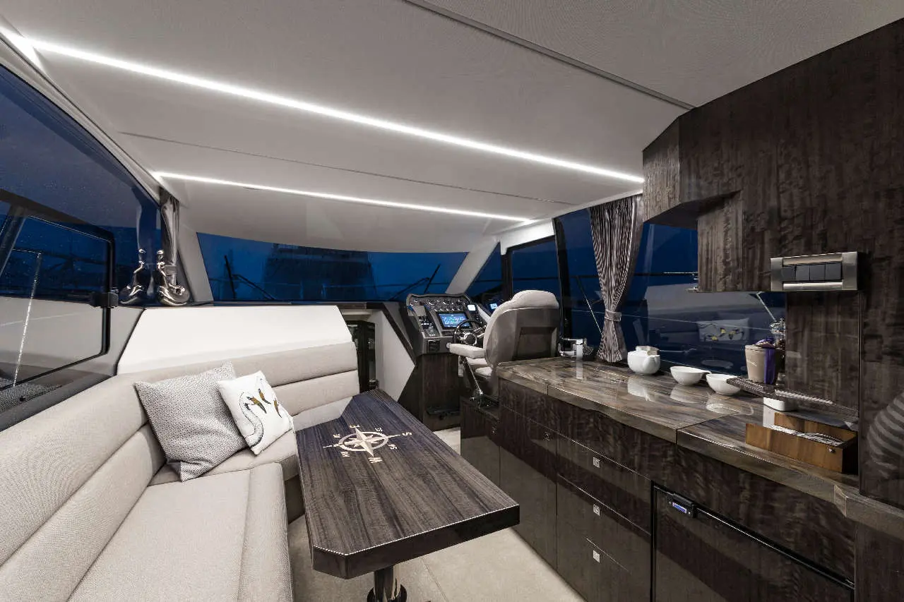 Luxurious yacht interior featuring a seating area, helm station, and modern cabinetry with night views through large windows.