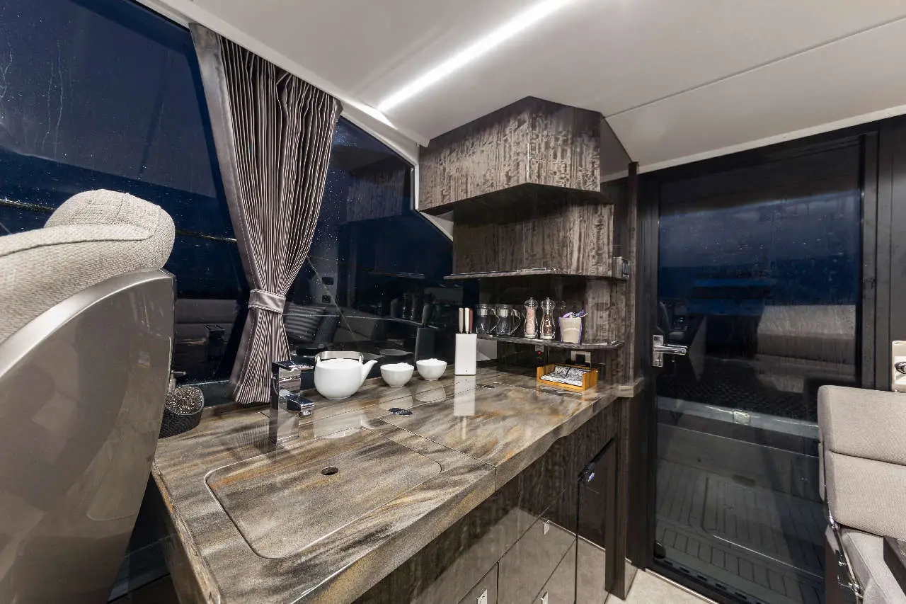 Modern yacht interior featuring a sleek kitchen area, dark cabinetry, a stylish grey chair, and water droplets on the windows.