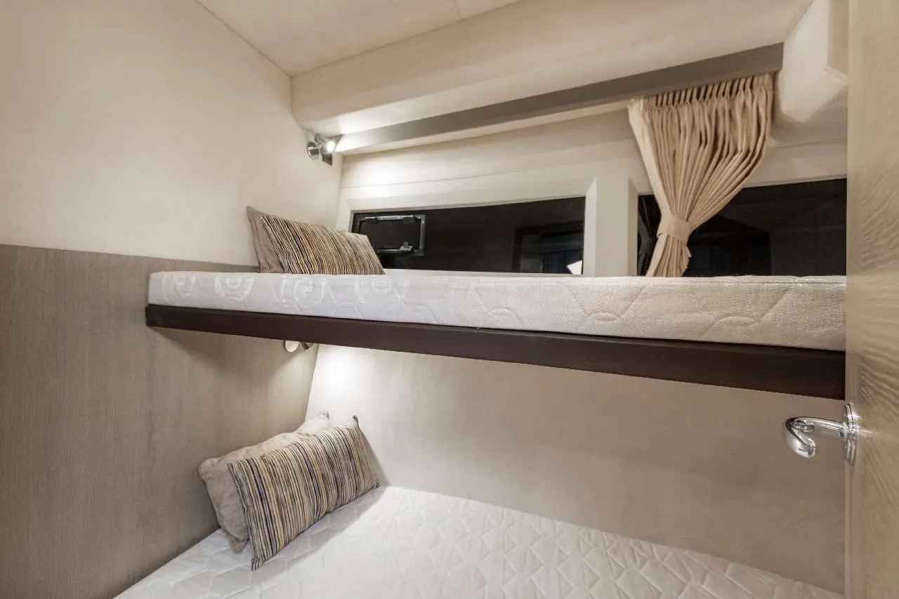 Bunk beds in a modern design with striped cushions, soft lighting, and a window, creating a cozy sleeping space.