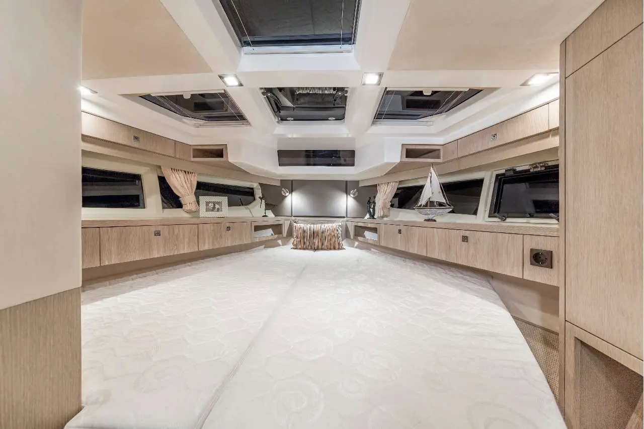 Modern yacht interior featuring light wood cabinetry, skylights, a large bed, and nautical decor with a model sailboat.