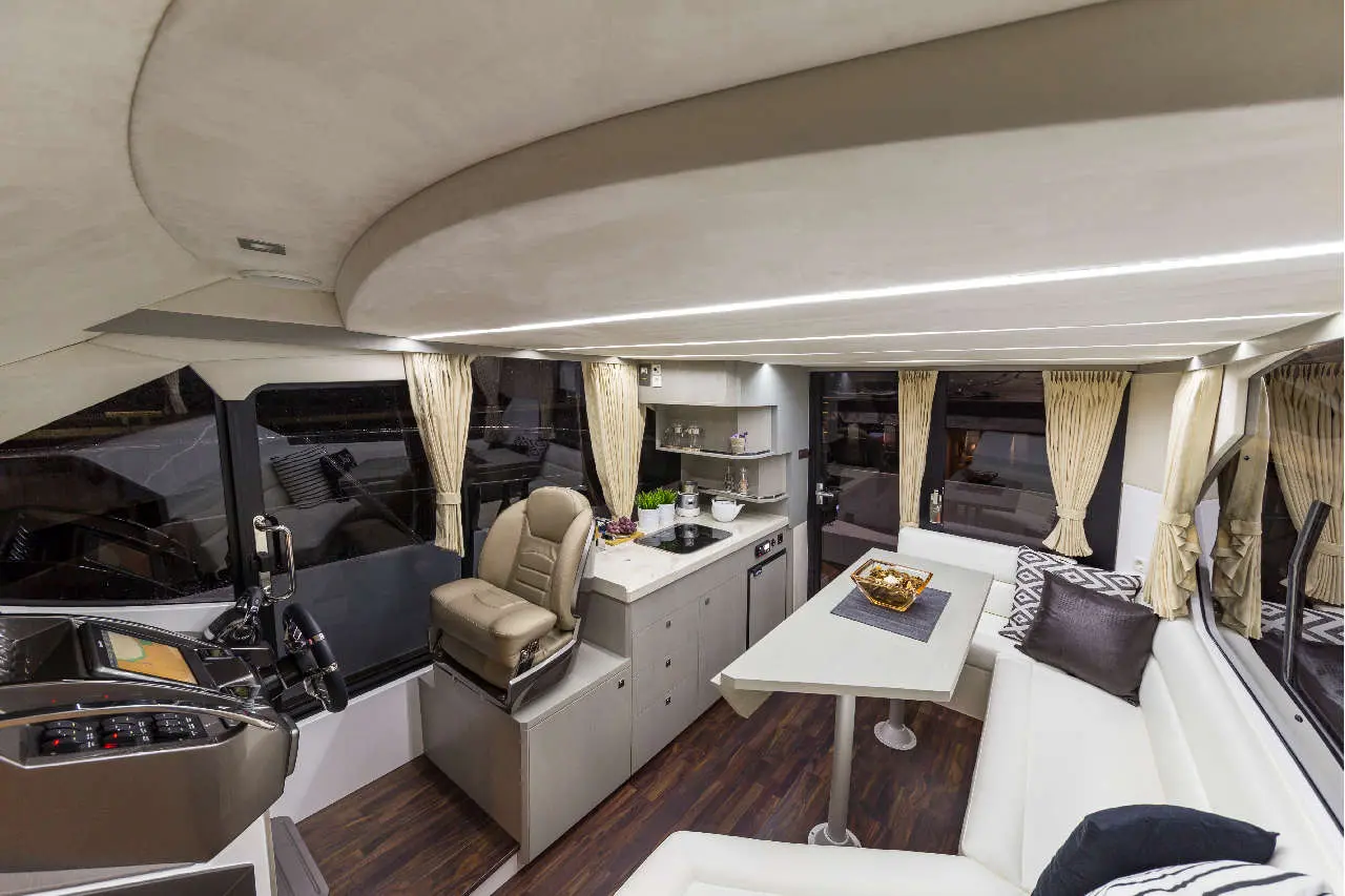 Modern yacht interior featuring a dining area, kitchen, control station, leather seating, and expansive windows with curtains.