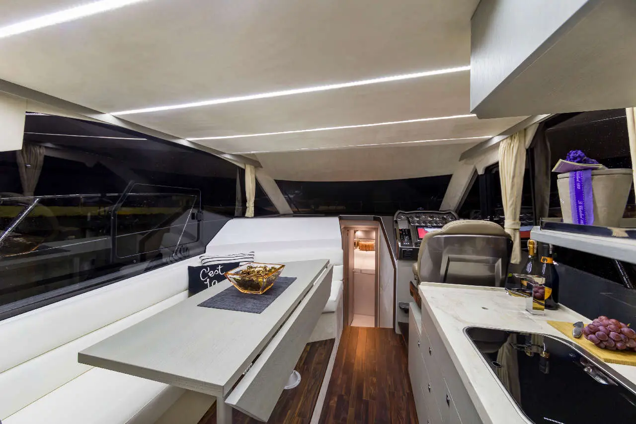 Modern yacht interior featuring a sleek dining area, navigation controls, and a cozy seating space, illuminated by soft lighting.