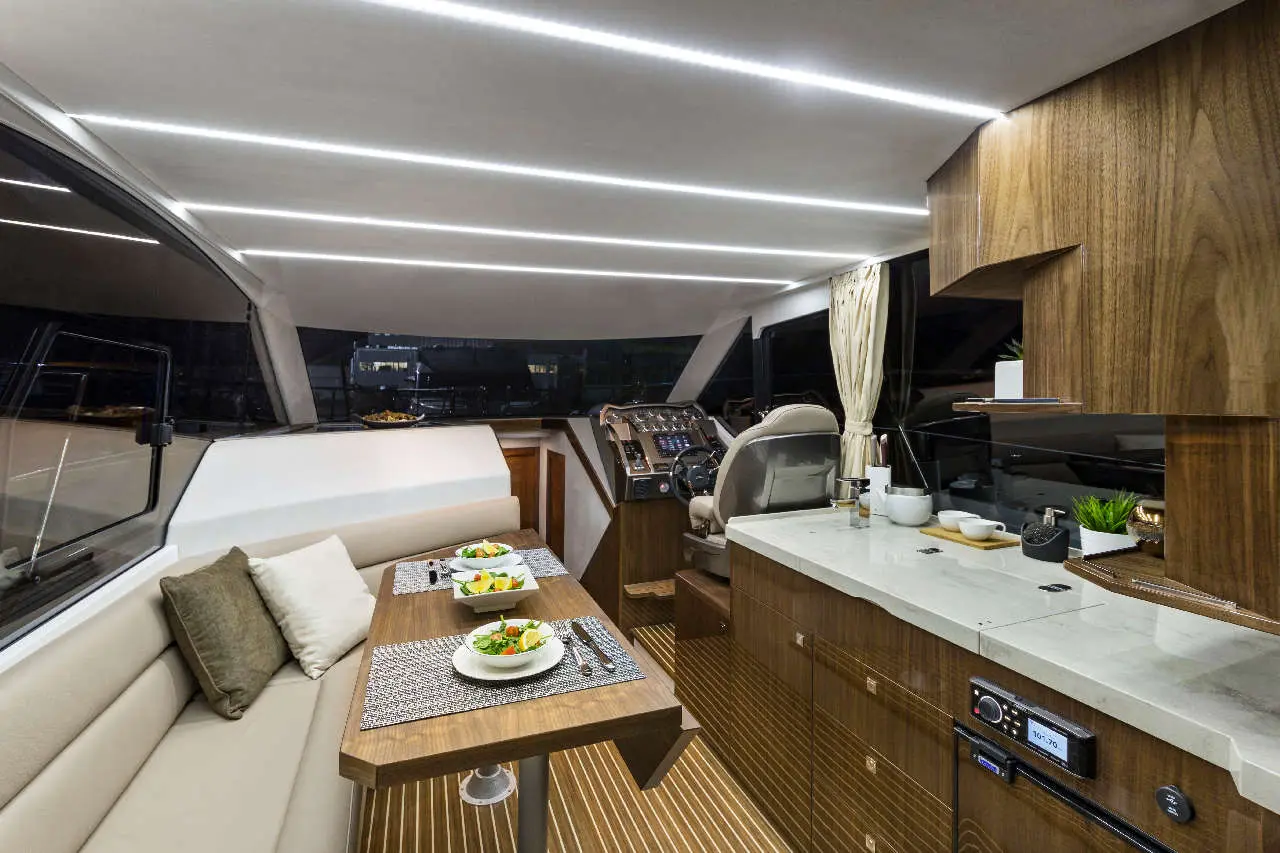 Luxurious yacht interior with a dining table set for two, modern controls, stylish cabinetry, and ambient lighting.