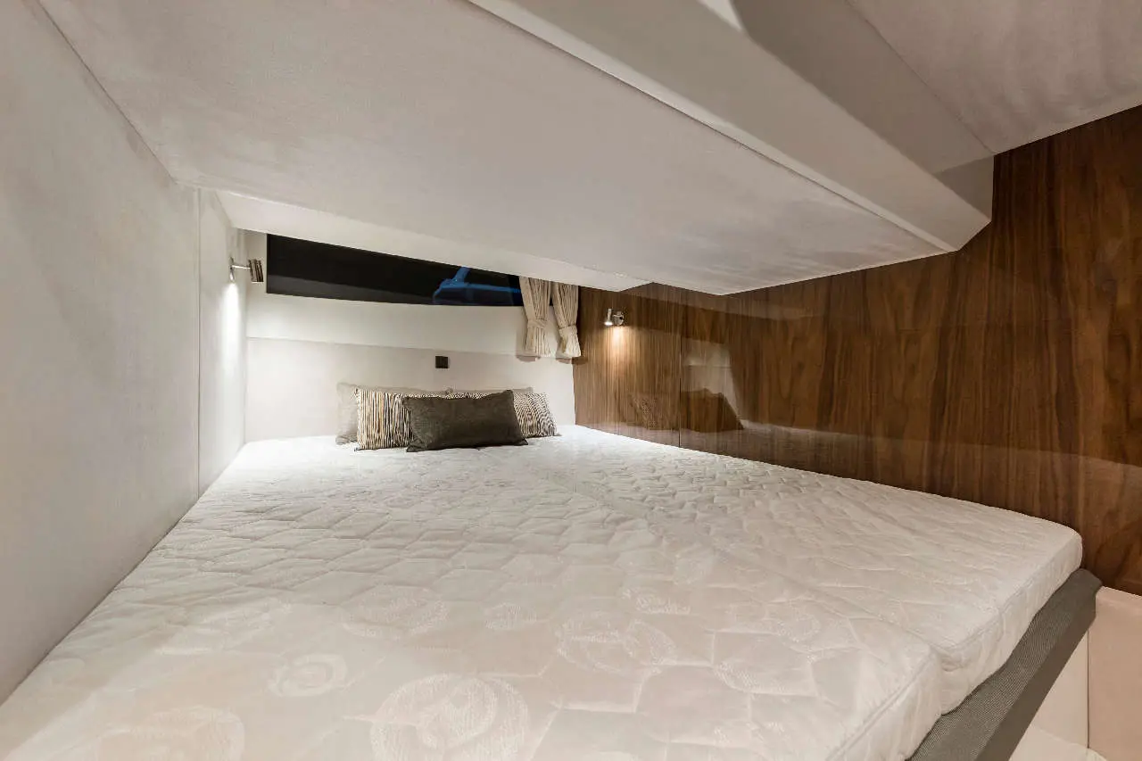 A compact bedroom with a double bed, wooden panel wall, and a small reading light, featuring striped decorative cushions.