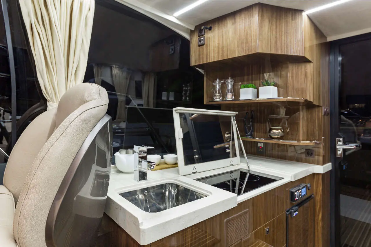 Modern boat interior featuring a kitchenette with a sink, countertop, and cooking area, complemented by wood paneling.