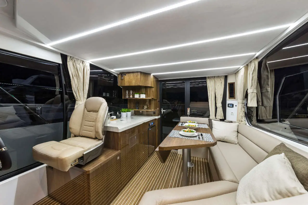 Luxurious boat interior featuring leather seating, modern kitchen, dining table with plates, and stylish lighting elements.