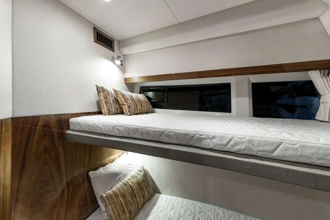 Bunk beds in a modern cabin, featuring striped cushions and soft lighting, with a view of the outside through windows.