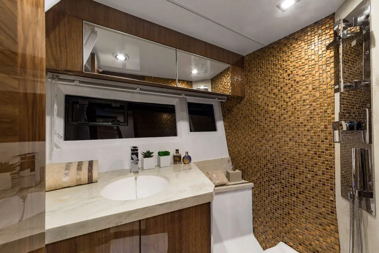 Modern boat bathroom featuring a stone sink, wooden cabinetry, mirrored shelving, and mosaic tiled wall for elegant design.