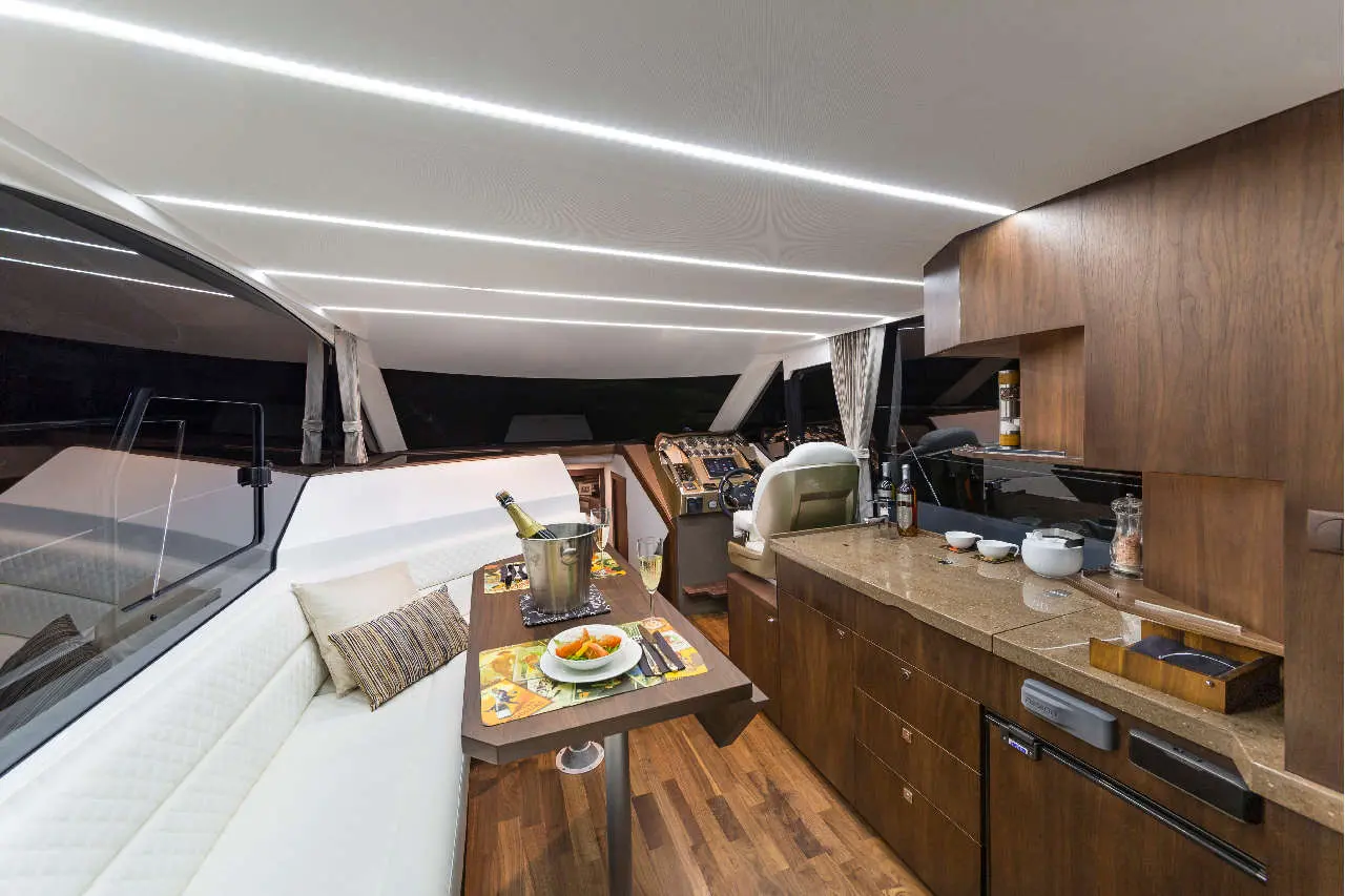 Modern yacht interior featuring a dining area, kitchen counter, and navigation station, with a champagne bottle and snacks.