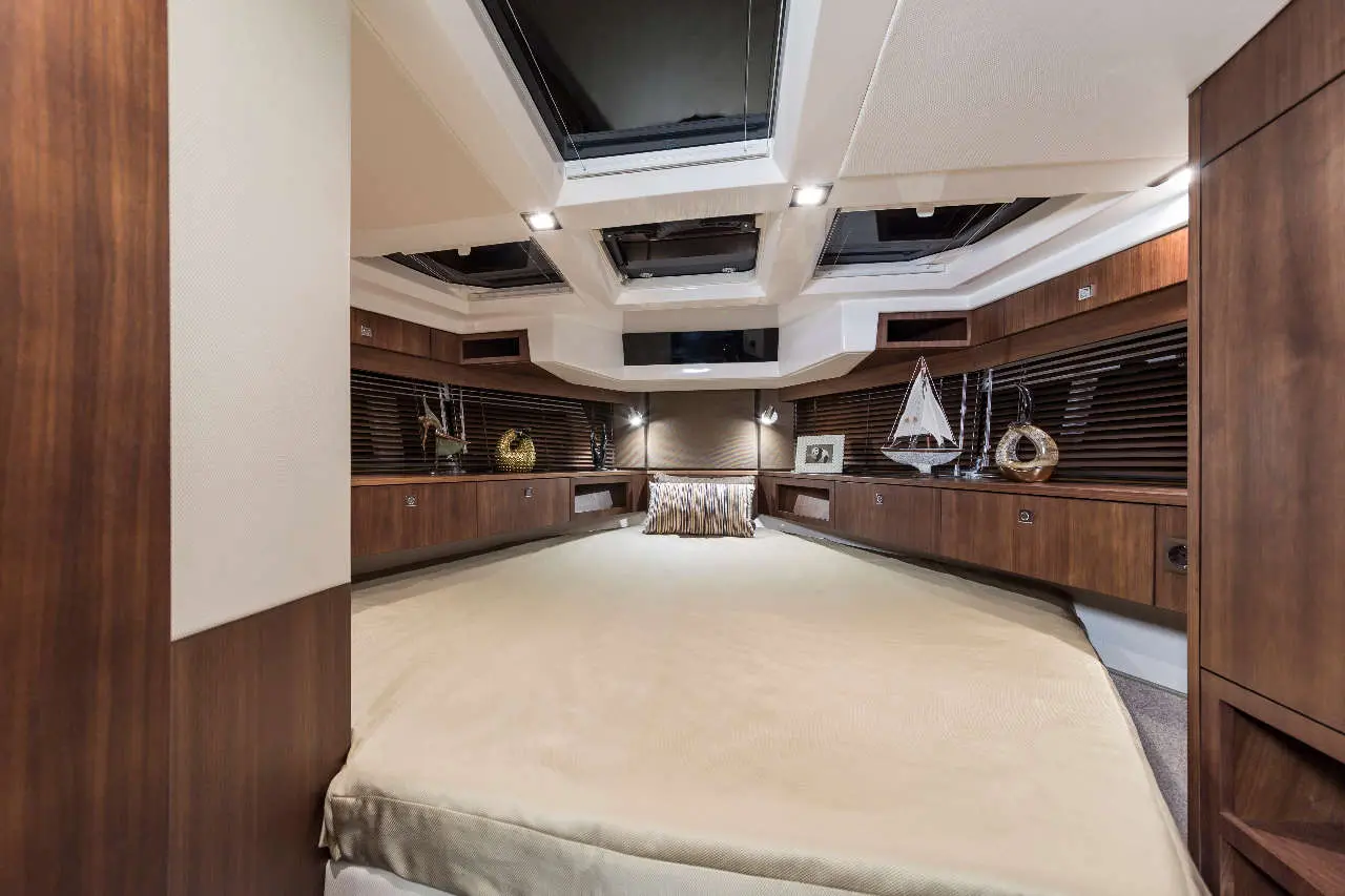 Luxury yacht interior featuring a spacious bedroom with wooden cabinetry and nautical decor, illuminated by skylights.