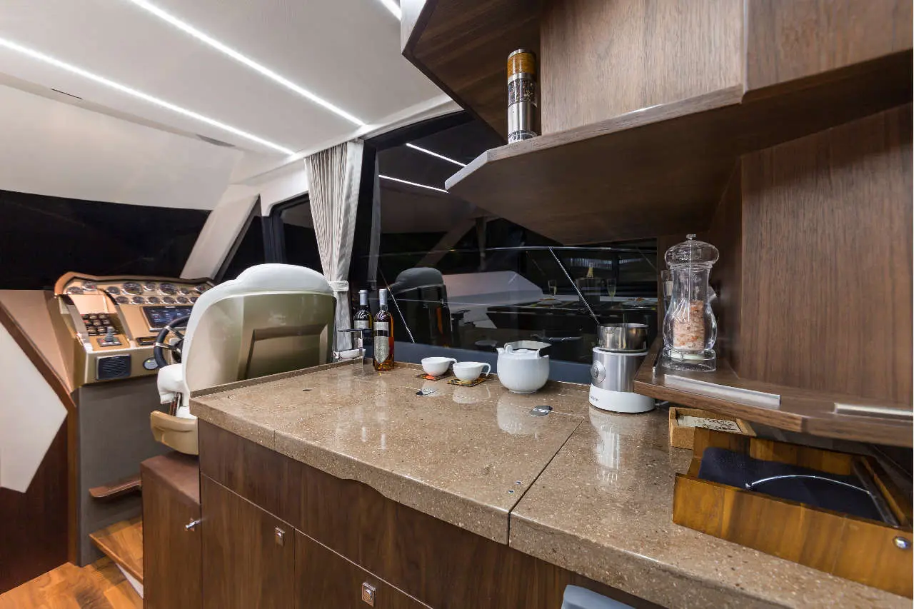 Interior of a luxury yacht showing a helm station, polished countertop with drinks, and a modern coffee maker.