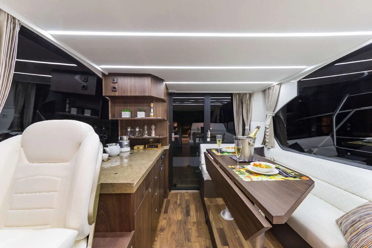 Luxurious yacht interior featuring a dining area, modern kitchen, and elegant decor, with a view of the water through large windows.