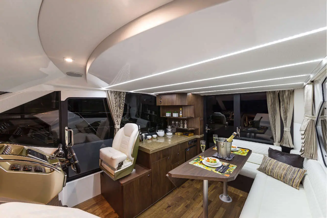 Stylish yacht interior featuring a dining area, kitchenette, and helm with modern lighting and elegant furnishings.
