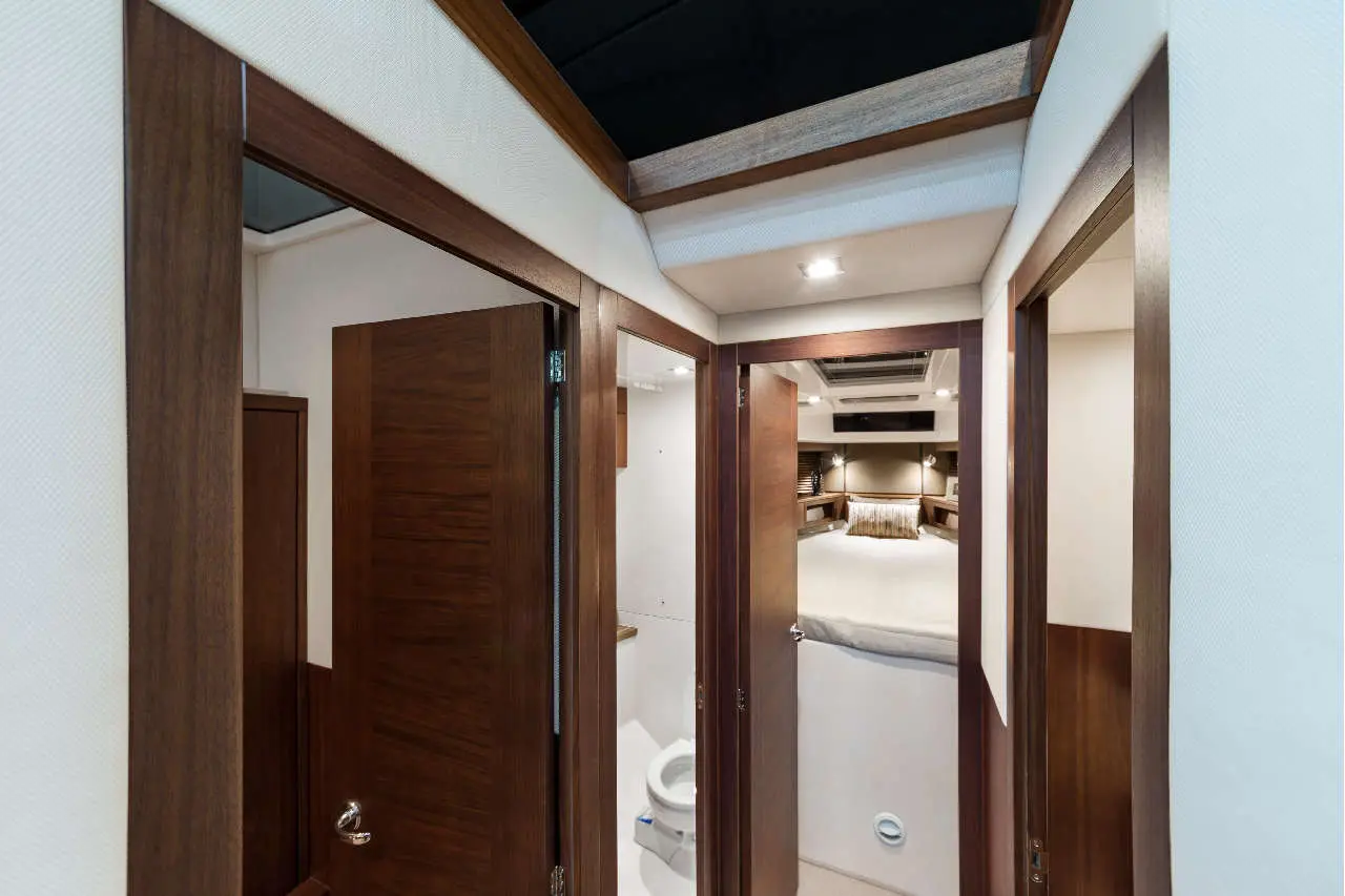 A modern yacht interior corridor with wooden doors leading to a bedroom and bathroom, featuring elegant furnishings and soft lighting.