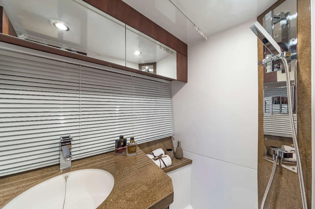 Modern bathroom featuring a stone sink, mirror, toiletries on the counter, and a shower with a chrome fixture and glass wall.