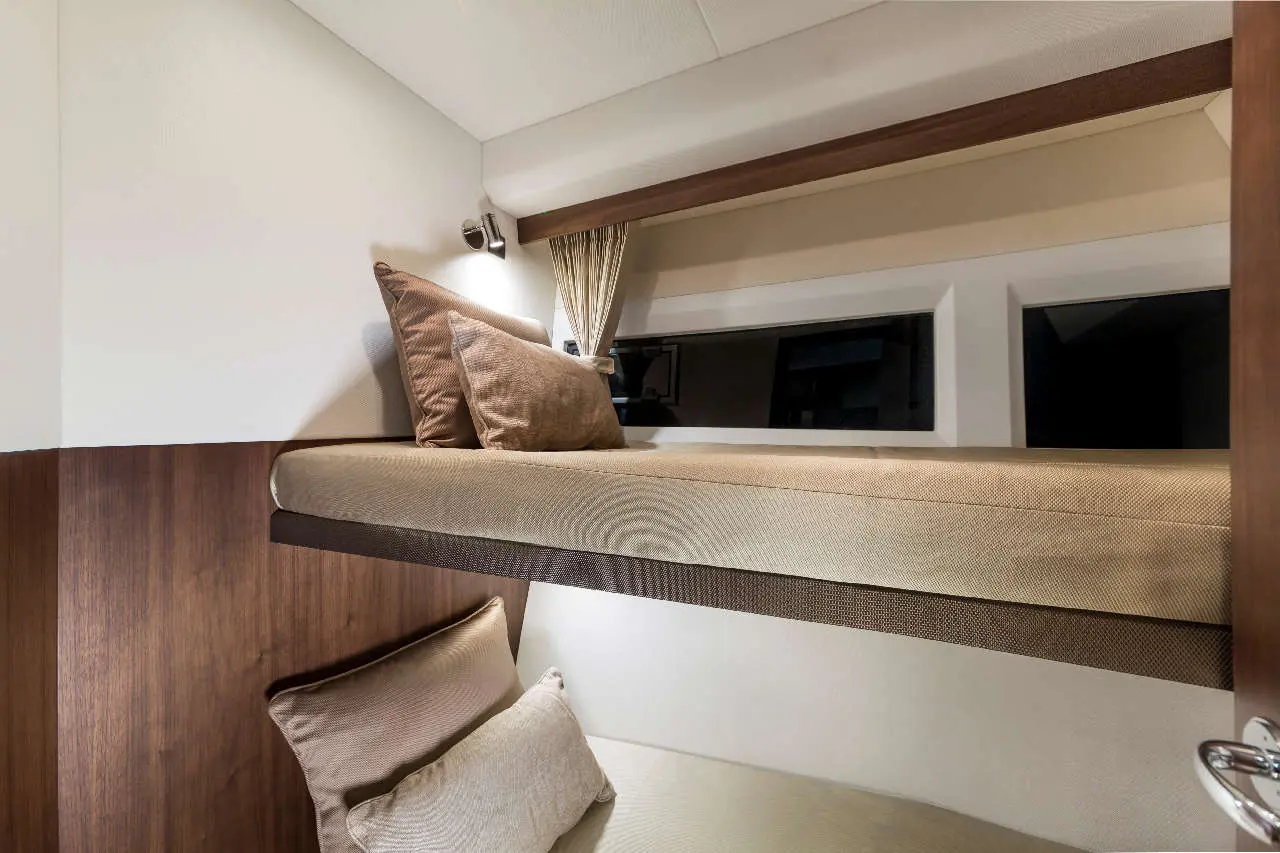 Cozy ship cabin with two stacked beds, decorative cushions, and a window, featuring warm wood accents and soft lighting.