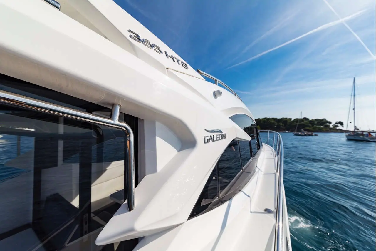 Luxury Galion 365 HTS yacht with sleek lines docked in clear blue waters, surrounded by sailing boats and greenery.