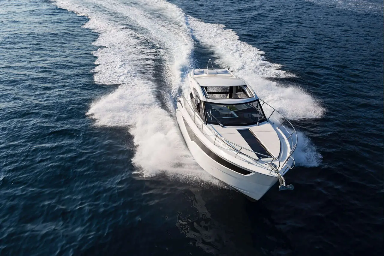 A sleek white motorboat moves swiftly across blue water, creating a spray of waves behind it in a sunny environment.
