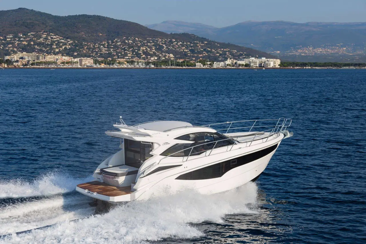 A sleek motorboat speeds through blue waters, with a coastal landscape and mountains in the background, showcasing luxury boating.
