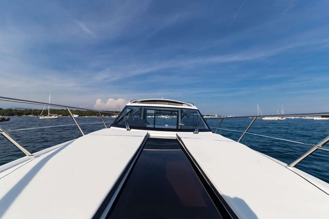 View from the bow of a white boat on calm water, with blue sky and distant boats in the background.