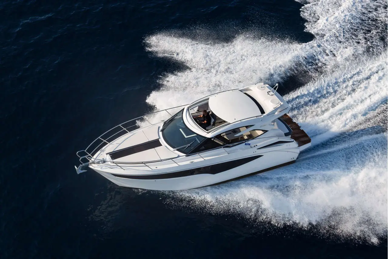 A luxury motorboat speeds through deep blue waters, leaving a trail of white foamy wake in its path.
