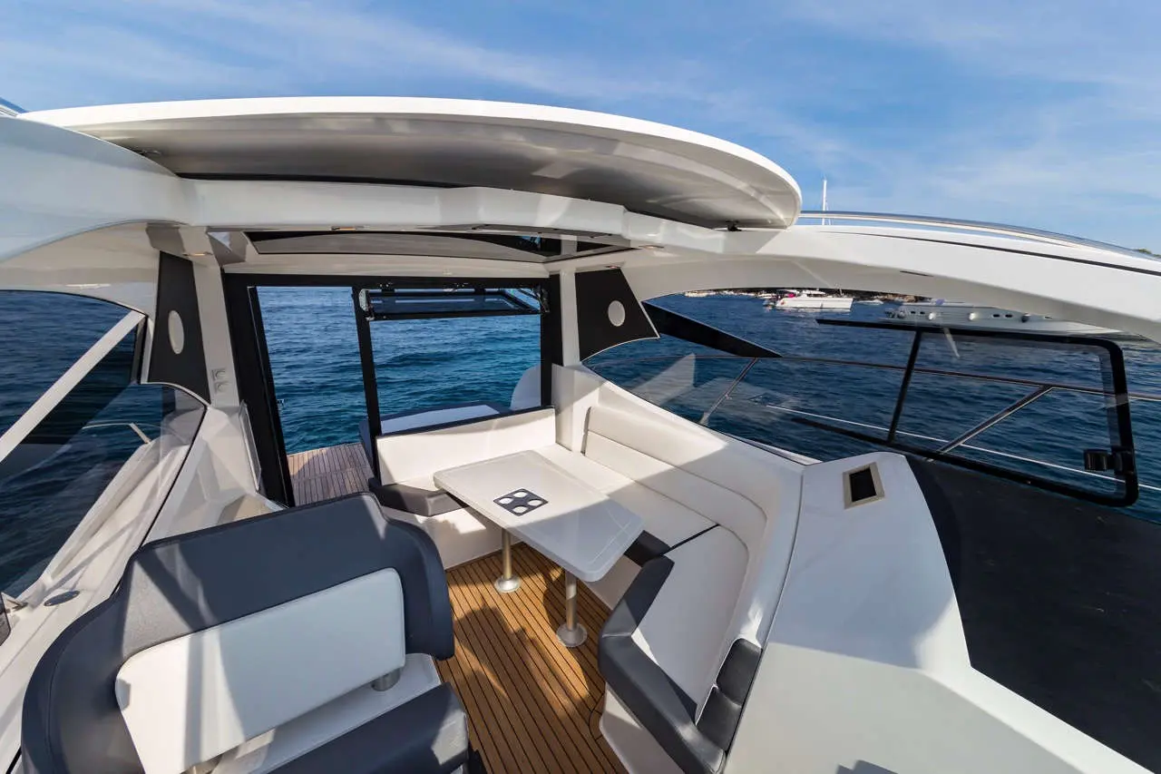Modern boat interior featuring a seating area, a table, and large windows with a view of the ocean and docked yachts.