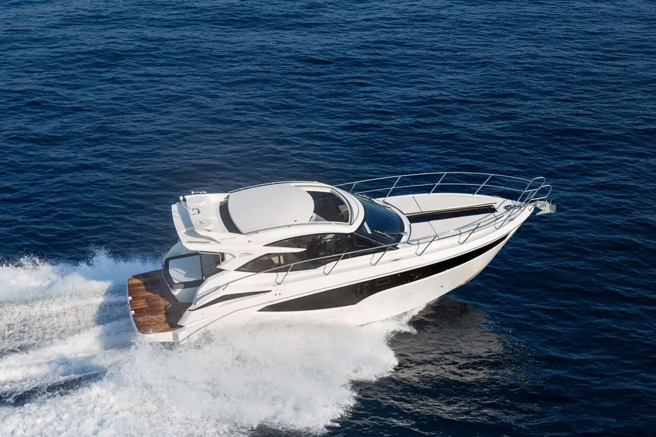 A sleek white motorboat cruising through deep blue waters, creating waves and foam behind it on a sunny day.