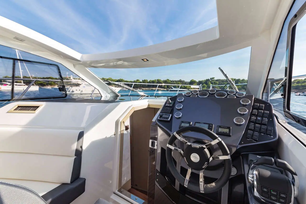 Luxury yacht cockpit with modern steering wheel and control panels, overlooking calm waters and distant green shoreline.