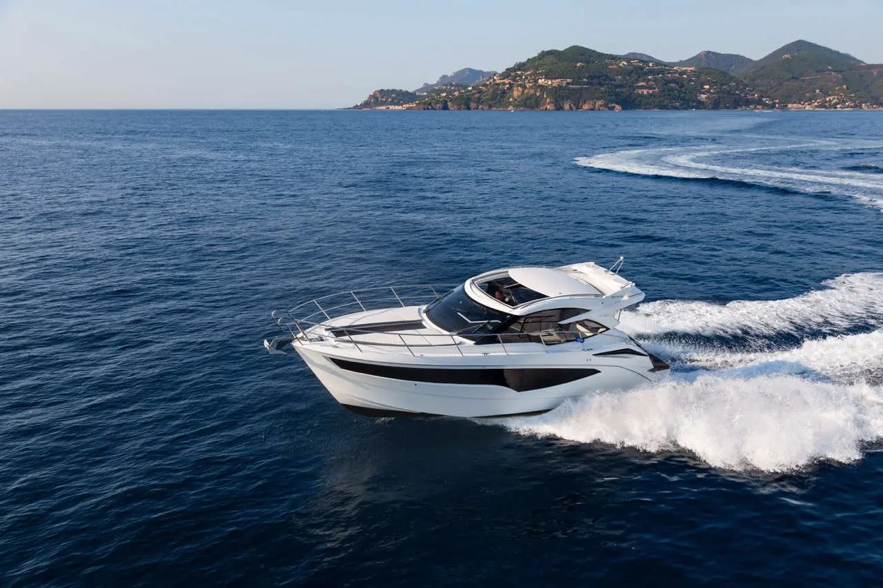 A sleek white motorboat cruising through blue waters with waves splashing, set against a coastal landscape.