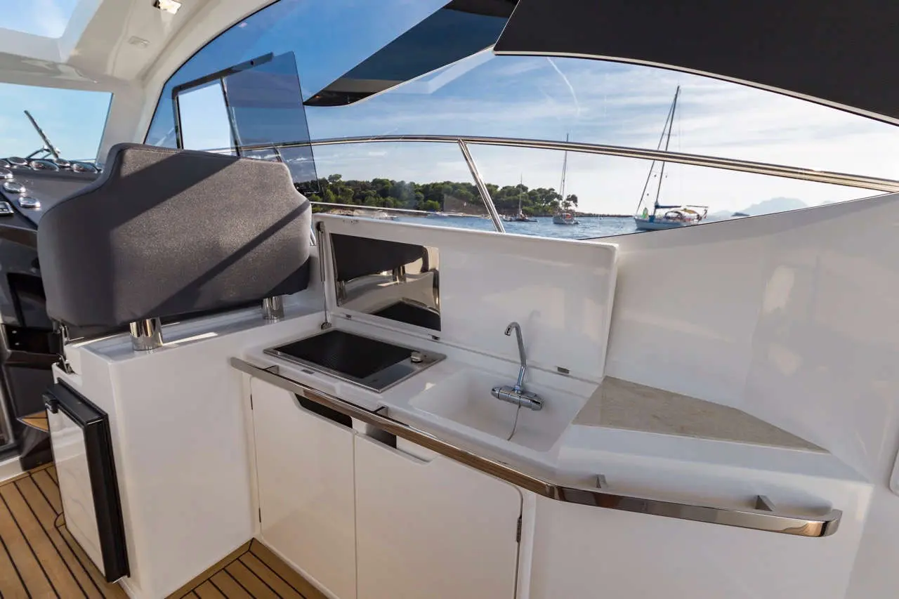 A modern yacht galley with a sink, cooking area, and a large window showing the marina and boats outside.