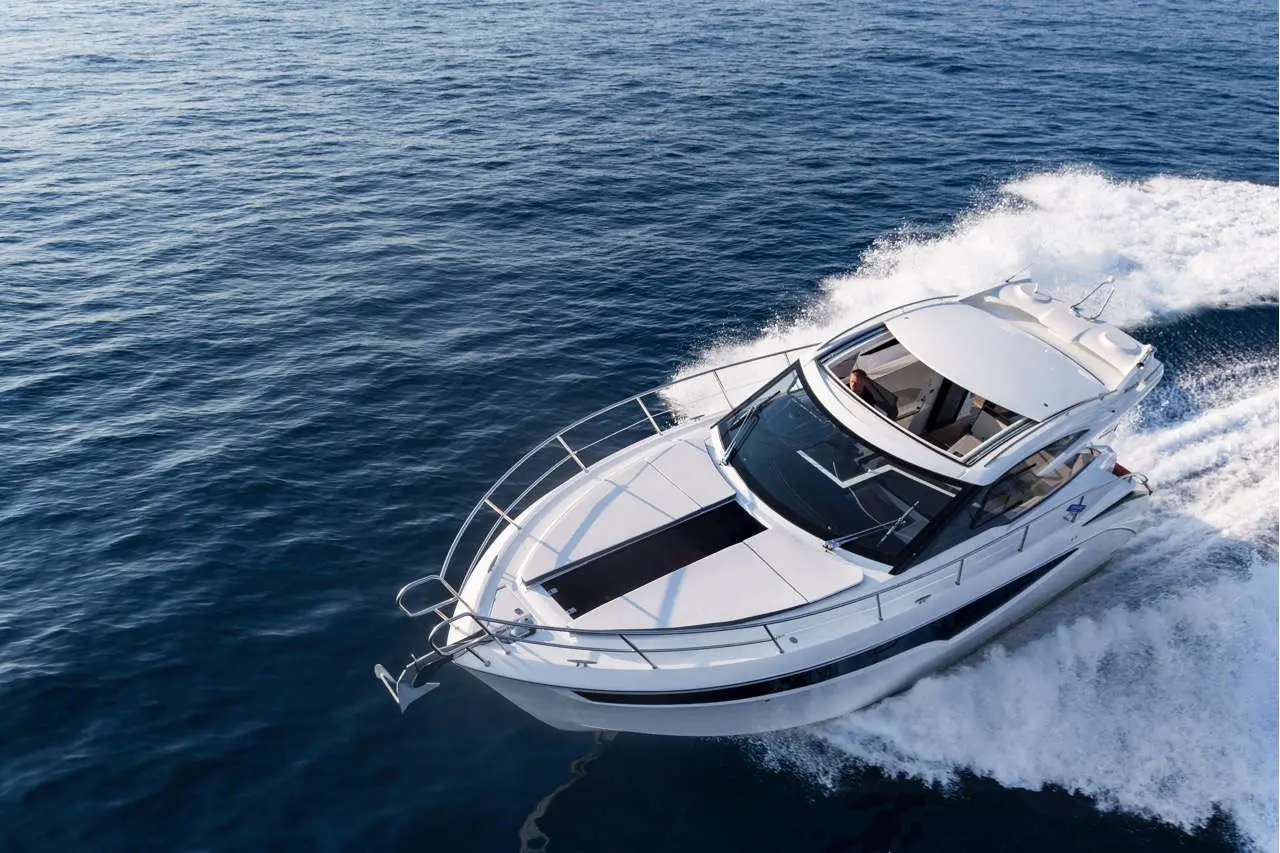 A white motorboat speeds through deep blue water, creating a wake, with a person visible at the helm.