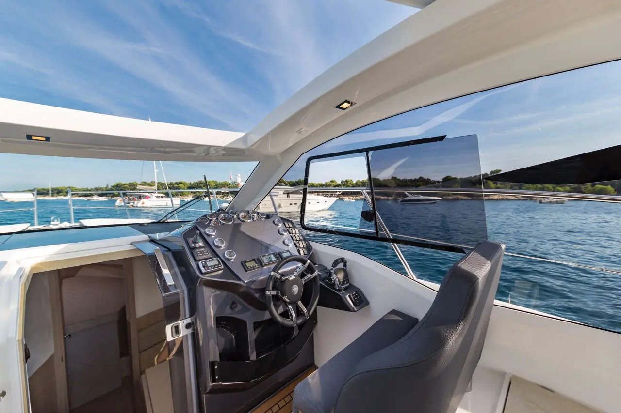 Luxury yacht cockpit featuring a steering wheel, control panel, and panoramic views of the marina and water.