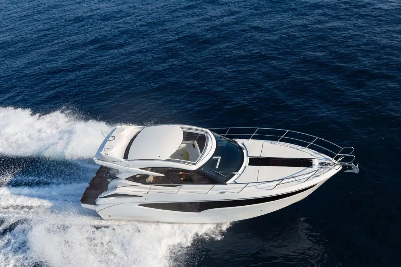 A sleek white motorboat speeds through calm blue waters, creating a white wake against the ocean surface.