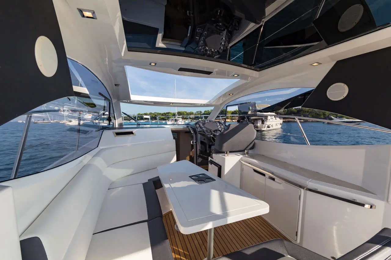 Modern yacht interior featuring a sleek seating area, navigation controls, and panoramic windows overlooking the marina.