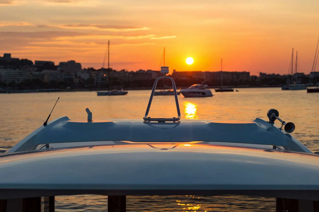 View from a boat's bow at sunset, with a golden sun setting over the water and silhouettes of moored boats in the background.