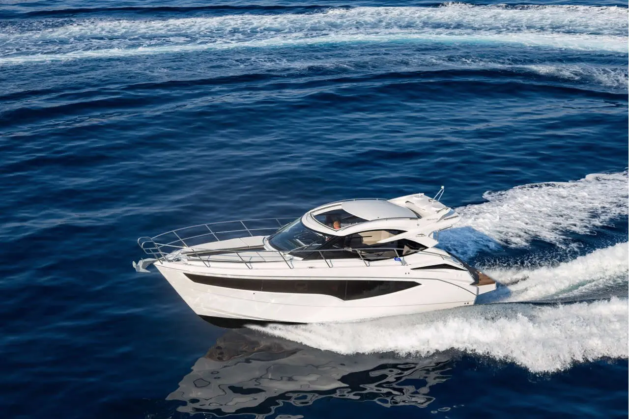 A sleek white motorboat navigates through deep blue waters, creating white waves in its wake.