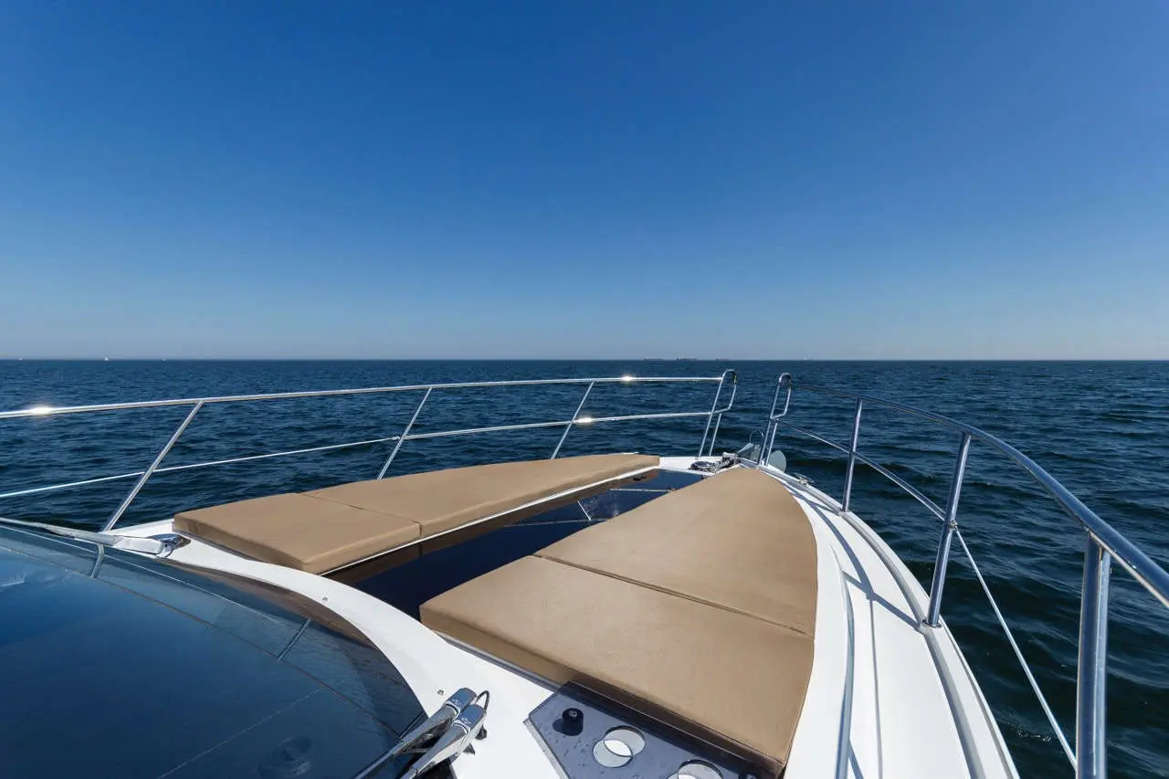 View from the bow of a boat, featuring tan cushions, blue ocean waves, and a clear blue sky.