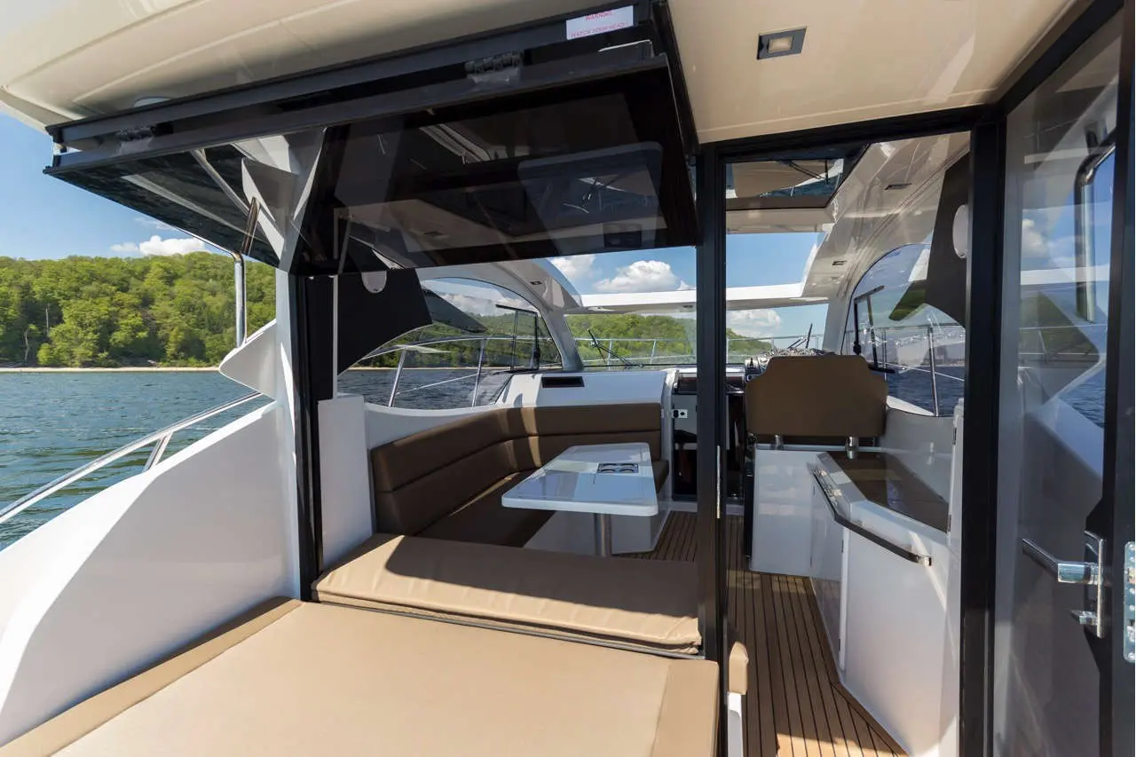 Interior of a luxury boat featuring a dining area with a table, plush seating, and windows overlooking a scenic water view.