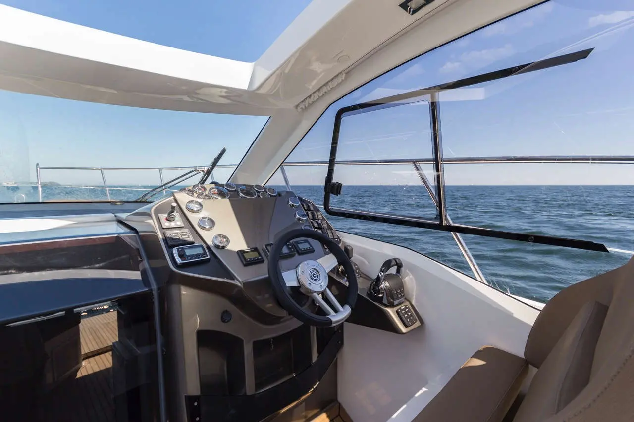 A yacht's steering console with gauges and controls, overlooking the sea under a clear blue sky.