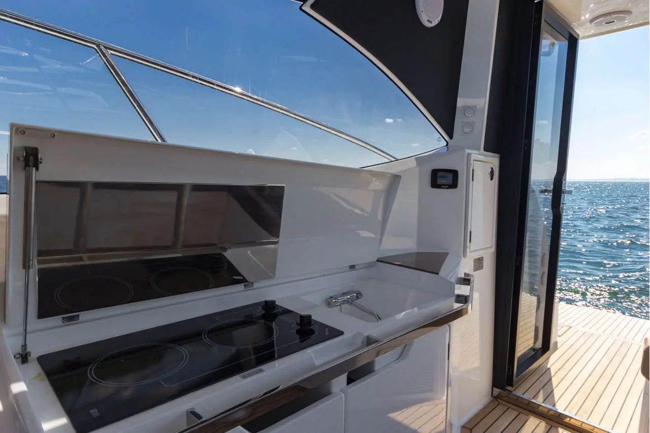 Modern boat kitchen featuring a countertop with two burners, sink, and a large window overlooking the water.
