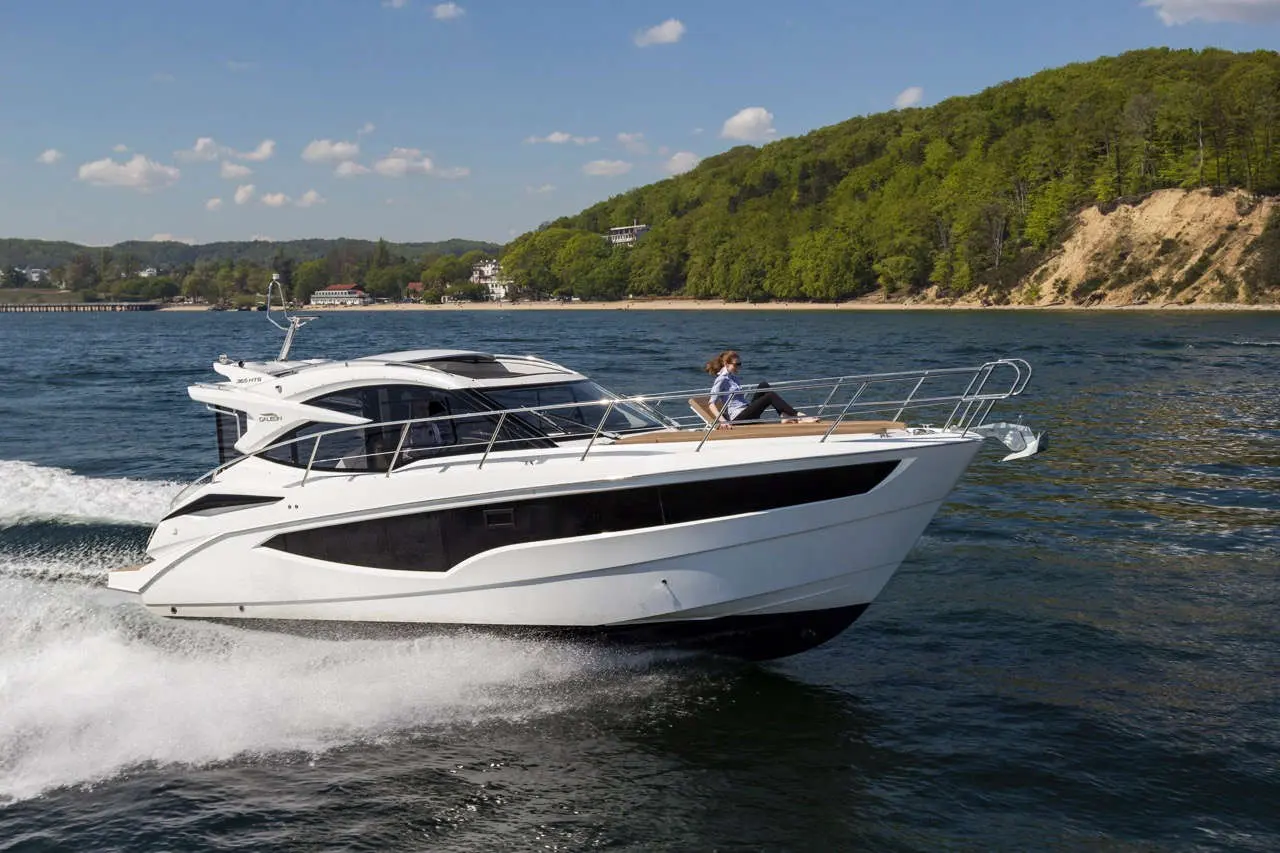 A sleek white motorboat cuts through the water, with a person seated comfortably on the deck, surrounded by green hills.