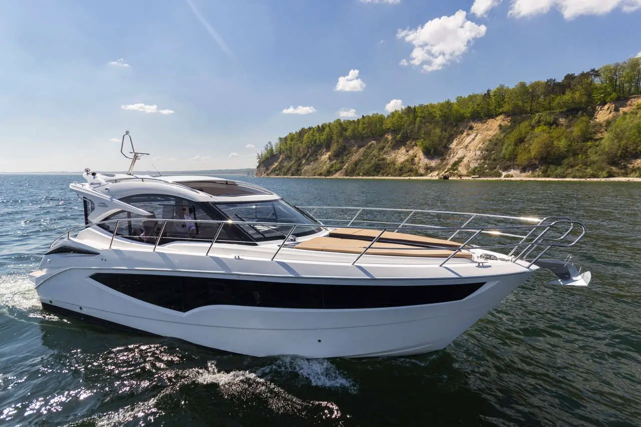 Luxury motor yacht cruising on calm waters, against a backdrop of lush green hills and blue sky with scattered clouds.