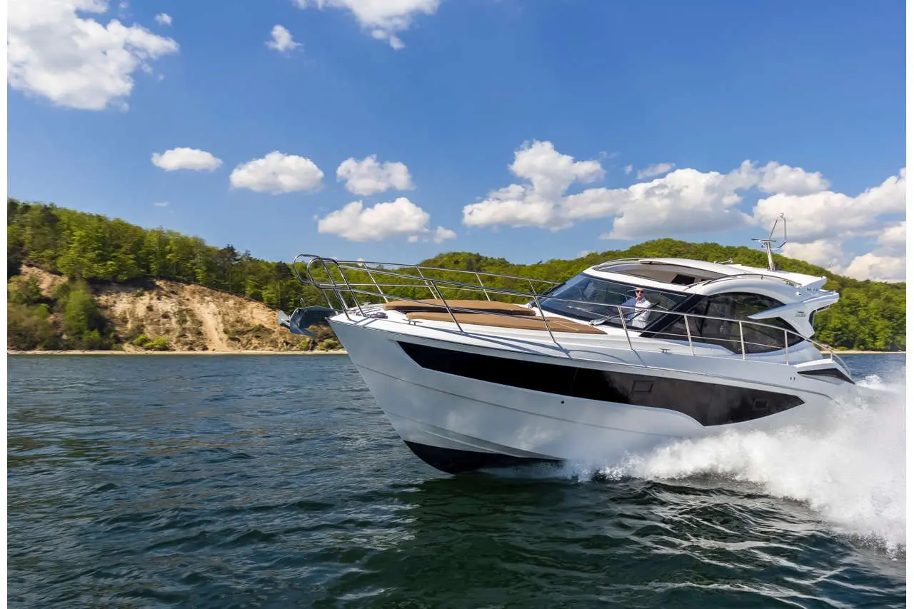 A sleek white motorboat navigates through clear blue water with green hills and clouds in the background, showcasing summer leisure.