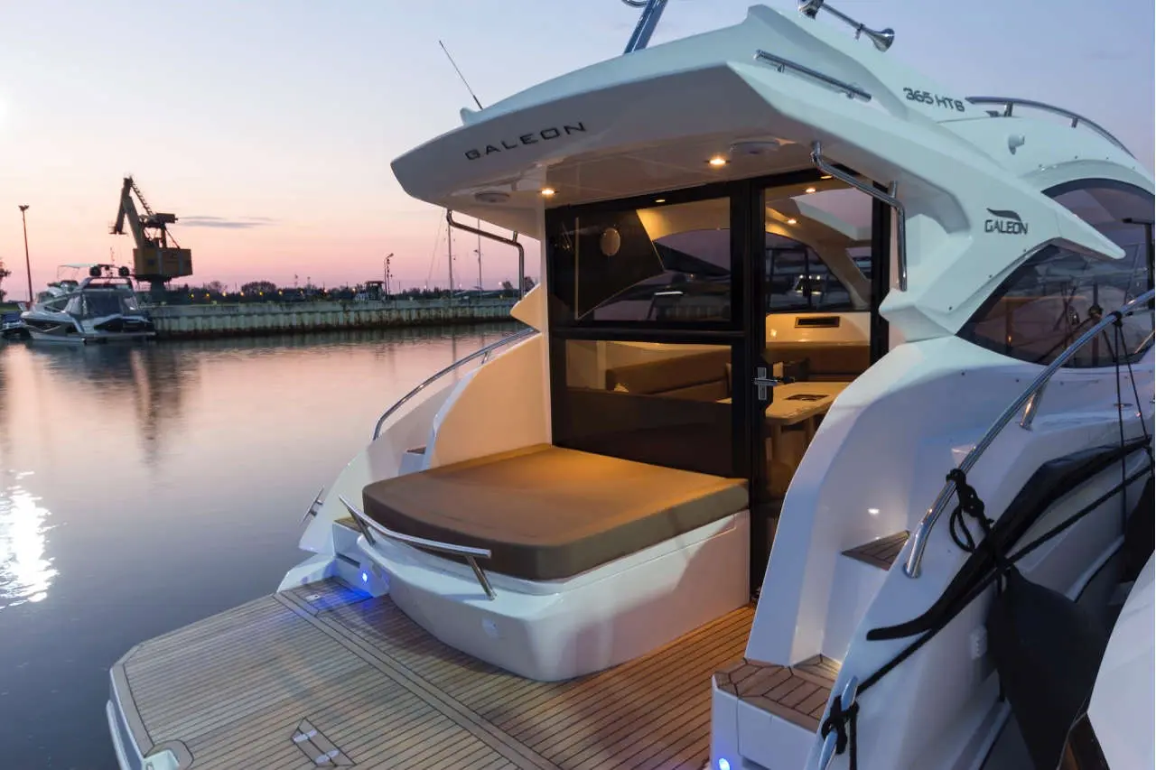 Luxury GALEON 365 HTB yacht in a marina at sunset, featuring a spacious deck and stylish interior with ambient lighting.
